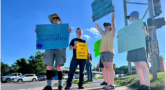 five people with signs about walkability on a sidewalk at a large intersection